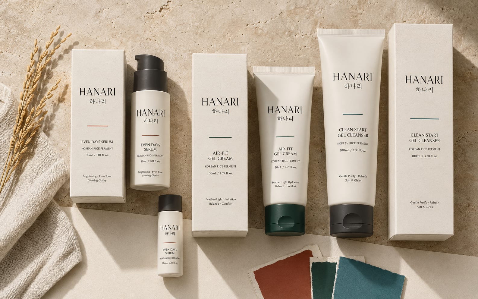 HANARI cartons and tubes arranged flat on linen beside rice stalks.